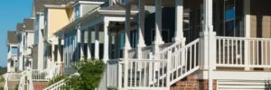 A row of modern two-story houses with front porches and manicured lawns on a clear day.