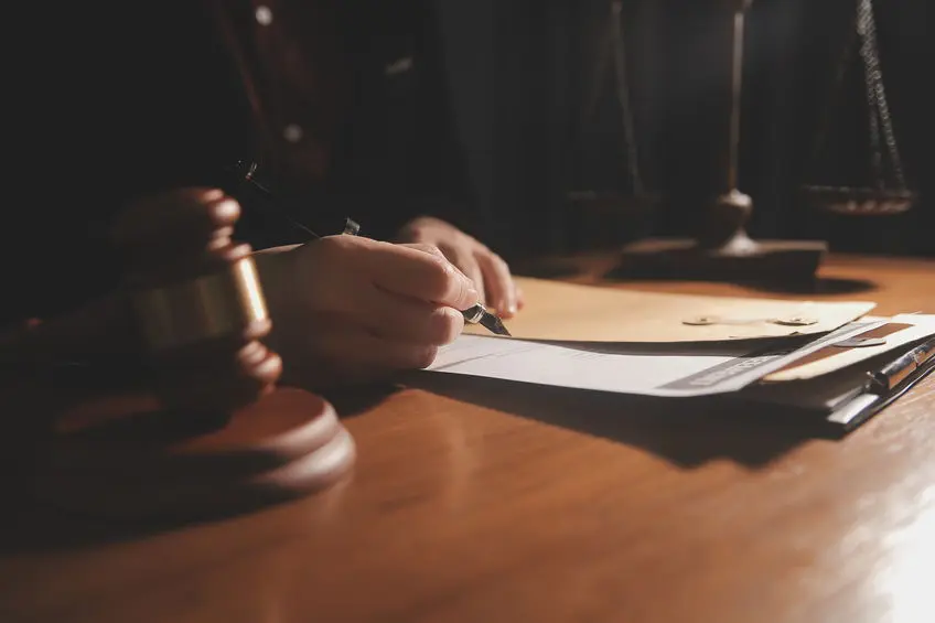 debt collection attorney discussing contract papers with brass scale on desk in office.